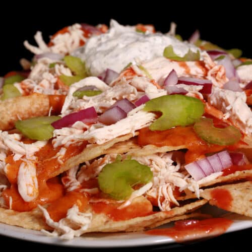 A platter of buffalo chicken nachos, with shredded chicken, Buffalo Wing nacho cheese sauce, hot sauce, red onions, celery, and ranch flavoured sour cream.