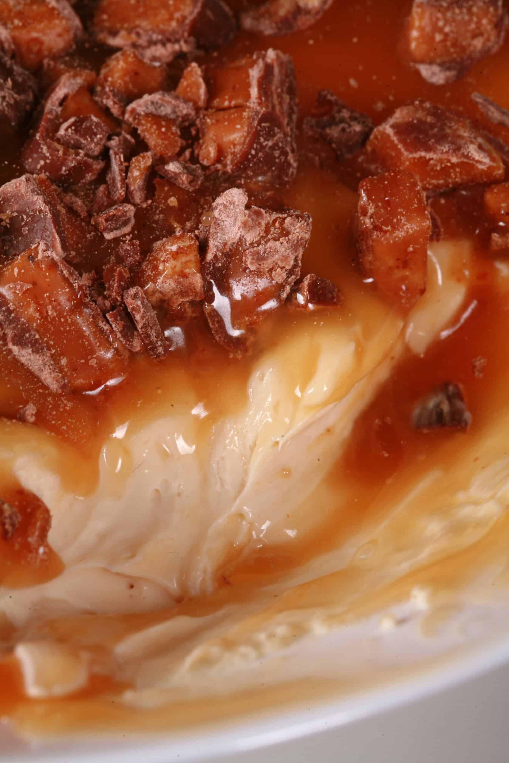 A bowl of caramel apple cheesecake dip, with caramel sauce and chopped Skor bars on top, and sliced granny smith apples behind it.