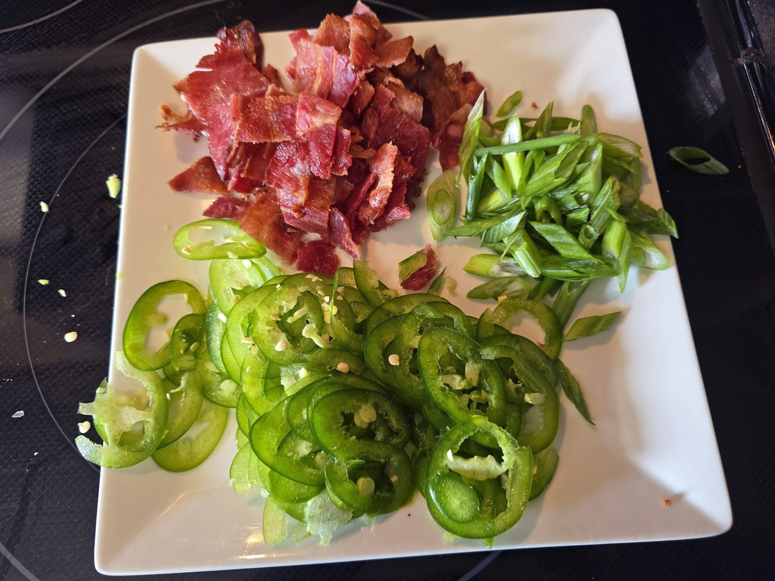 A plate of thinly sliced jalapenos, green onions, and chopped bacon.