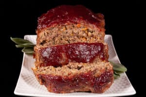 Venison meatloaf with carrots, mushrooms, celery bits, and herbs visible, topped with cranberry glaze.