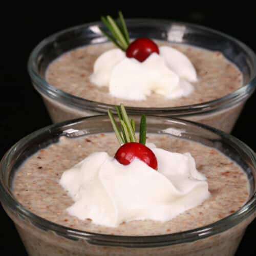 2 glass bowls of eggnog chia pudding garnished with whipped cream, a cranberry, and a sprig of rosemary.