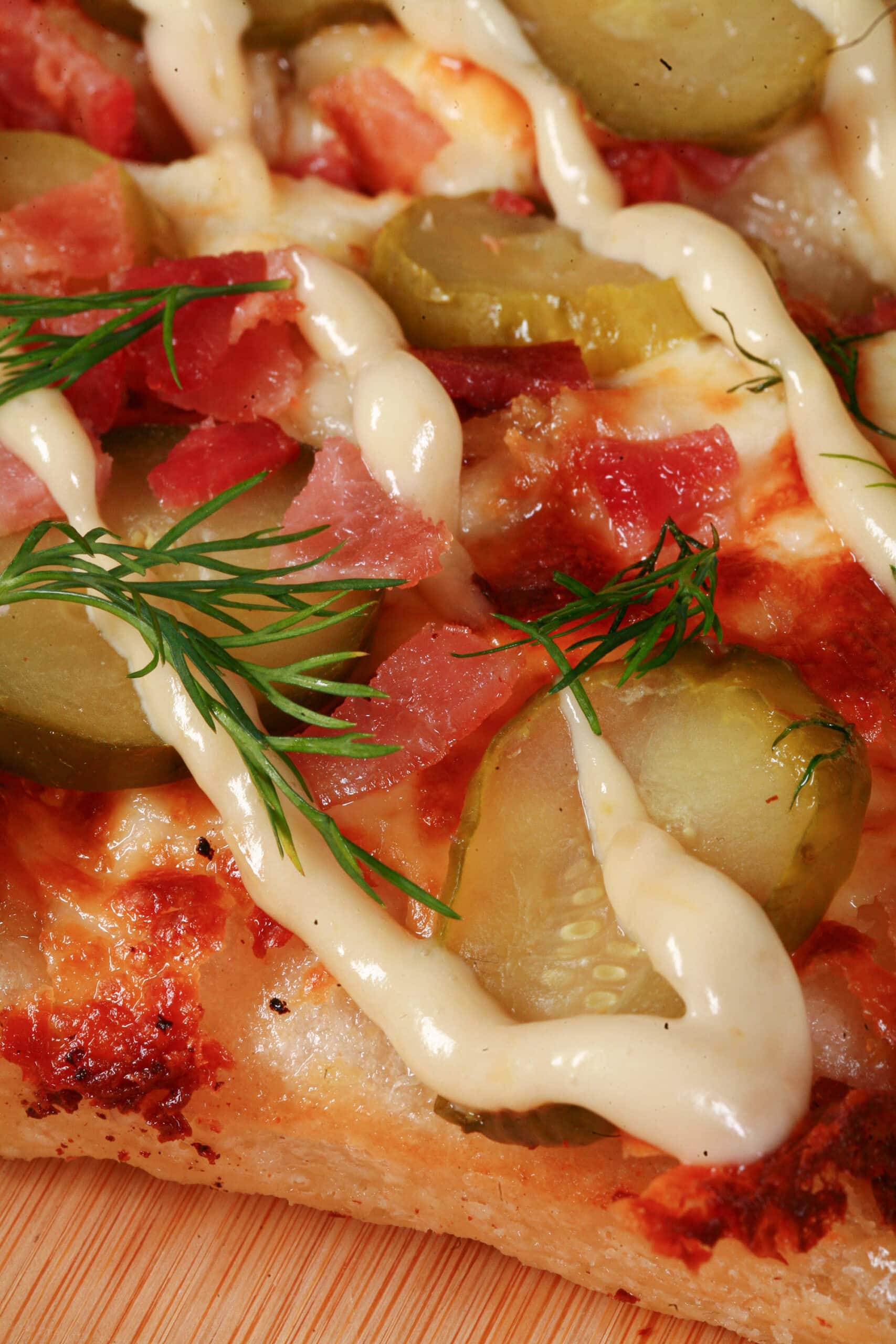 A detroit style gluten free dill pickle pizza, with pickle slices, bacon, fresh dill, and roasted garlic mayonnaise drizzled across it.